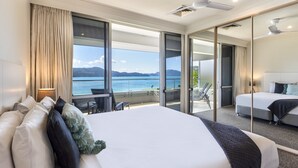 Une chambre d’hôtel dotée d’un grand lit, d’un balcon avec vue sur la mer et d’un coin salon séparé avec un fauteuil et une table.
