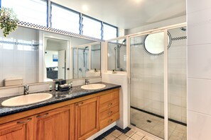 A modern bathroom with two sinks, wooden cabinets, and a glass-enclosed shower area. - Frangipani 201 Hamilton Island by HamoRent (Hamilton Island)