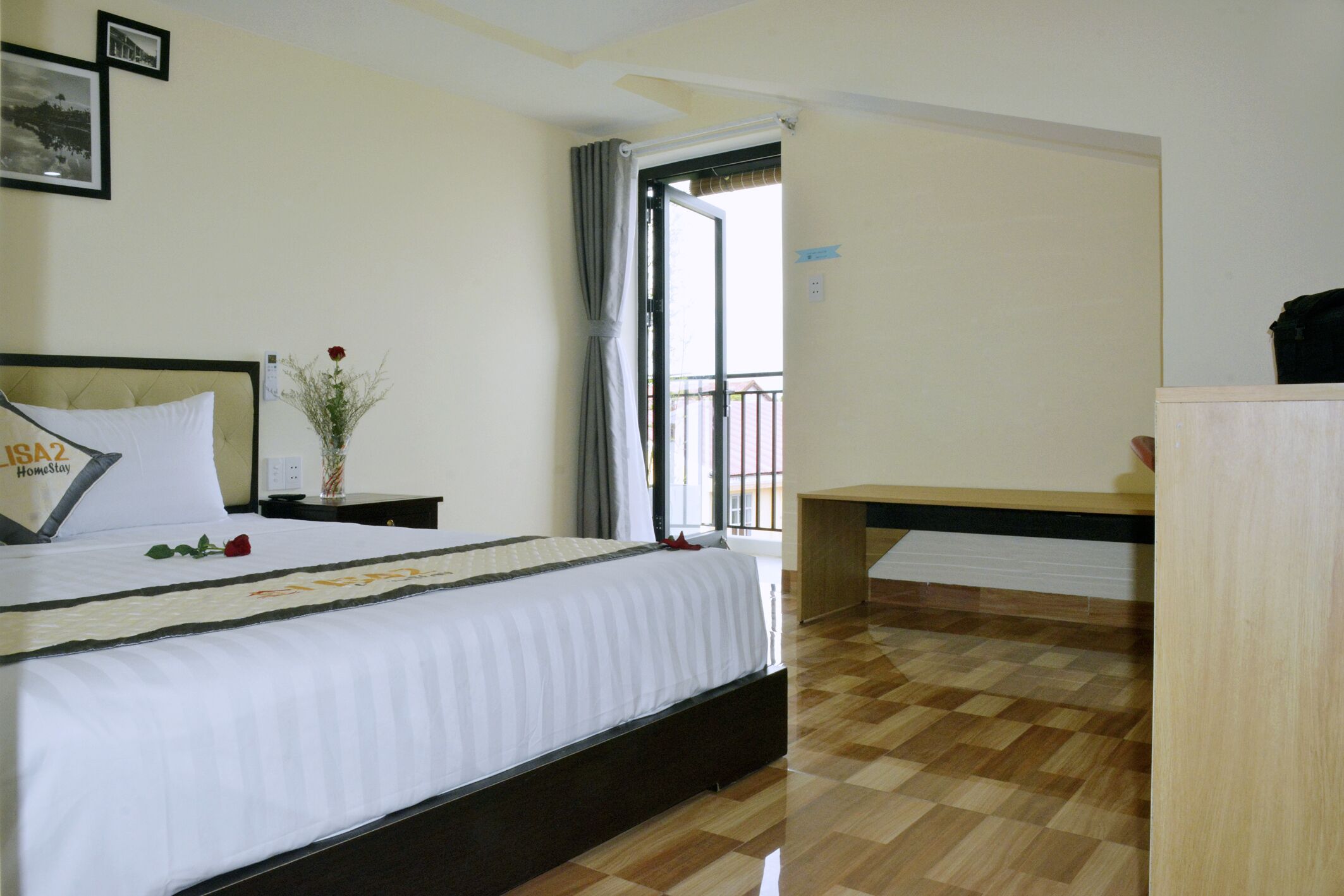A hotel room with a bed, a nightstand, a bedside table, a wooden desk, and a balcony door.