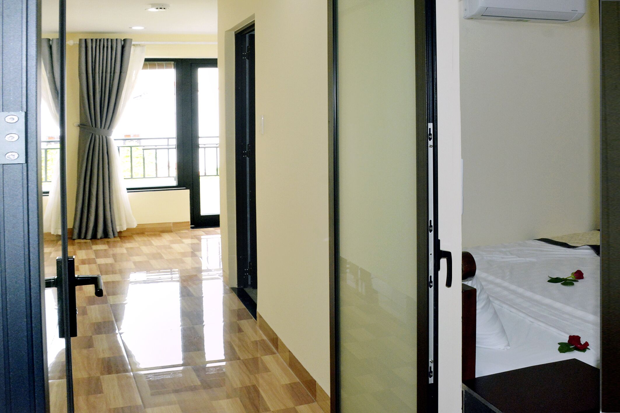 A hotel room with a checkered floor, a bed with white bedding and red roses, a door with a handle, and a window with curtains.