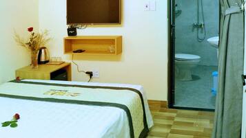A hotel room with a bed, a TV, a shower, and a wooden floor.