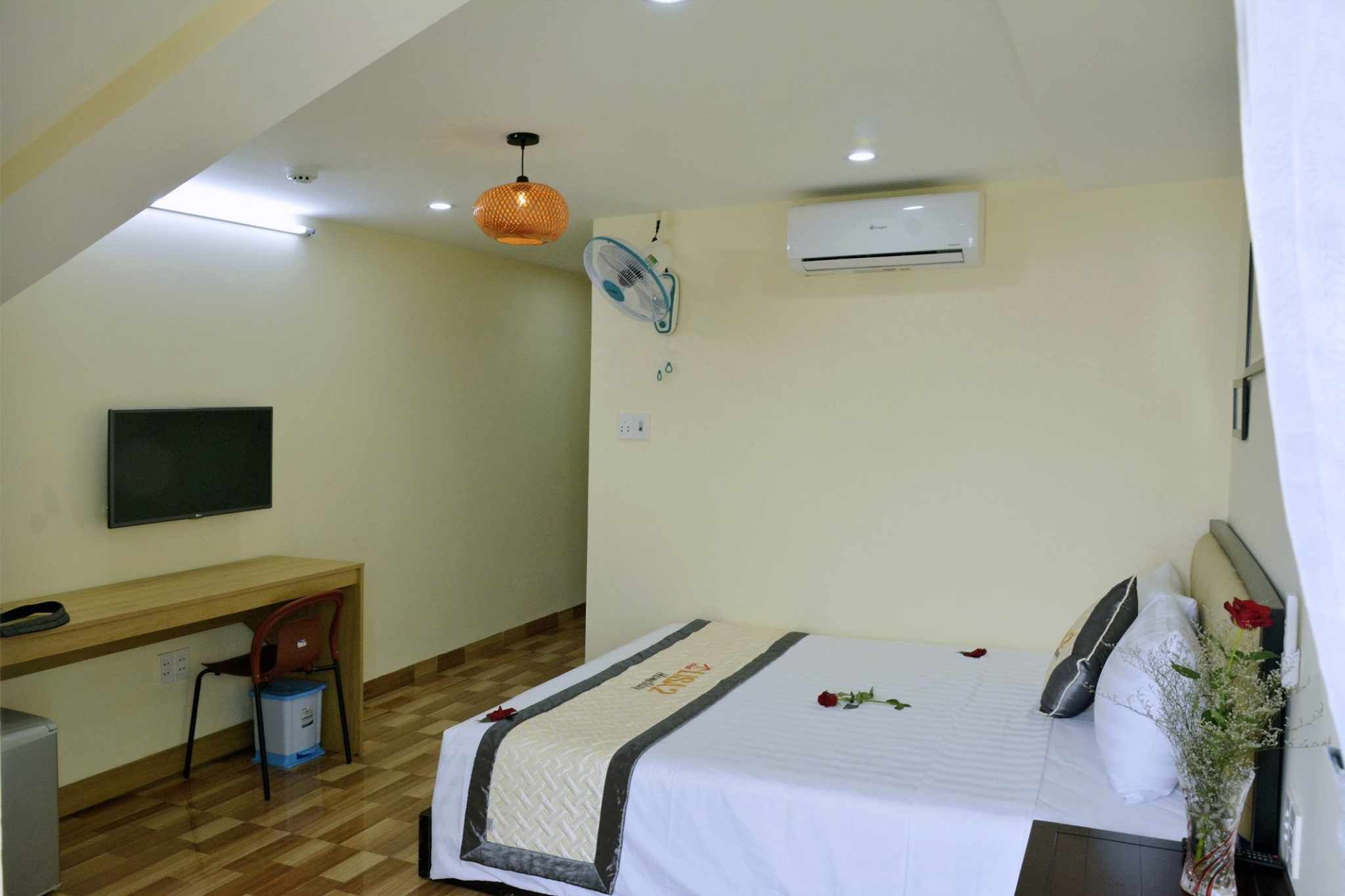 Ein Hotelzimmer mit einem Bett, einem Schreibtisch, einem Sessel, einem Fernseher, einer Klimaanlage und einem Deckenventilator.