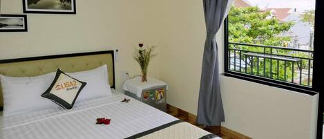 A hotel room with a bed, a nightstand, a window with a view of greenery, and a wall with framed pictures.
