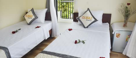 A hotel room with two beds, each with a white bedspread and a pillow featuring the hotel's logo. There are rose petals on the beds, and a refrigerator is visible in the corner.