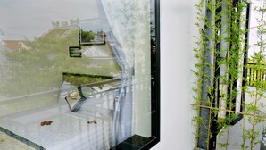 A modern interior with a large window reflecting a street scene, a small indoor garden with bamboo, and a white wall. - Lisa Homestay 2 (Da Nang)