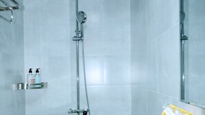 A bathroom with a toilet, a sink with rose petals, a shower, and a glass shelf with toiletries. - Lisa Homestay 2 (Da Nang)