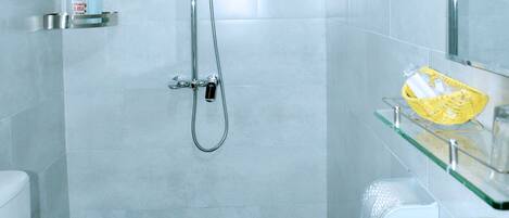 Un baño con inodoro, lavamanos decorado con pétalos de rosa, ducha y estante de vidrio con artículos de tocador.