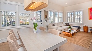 Un salon spacieux avec une grande table à manger, des sièges confortables et de grandes fenêtres donnant sur l’extérieur.