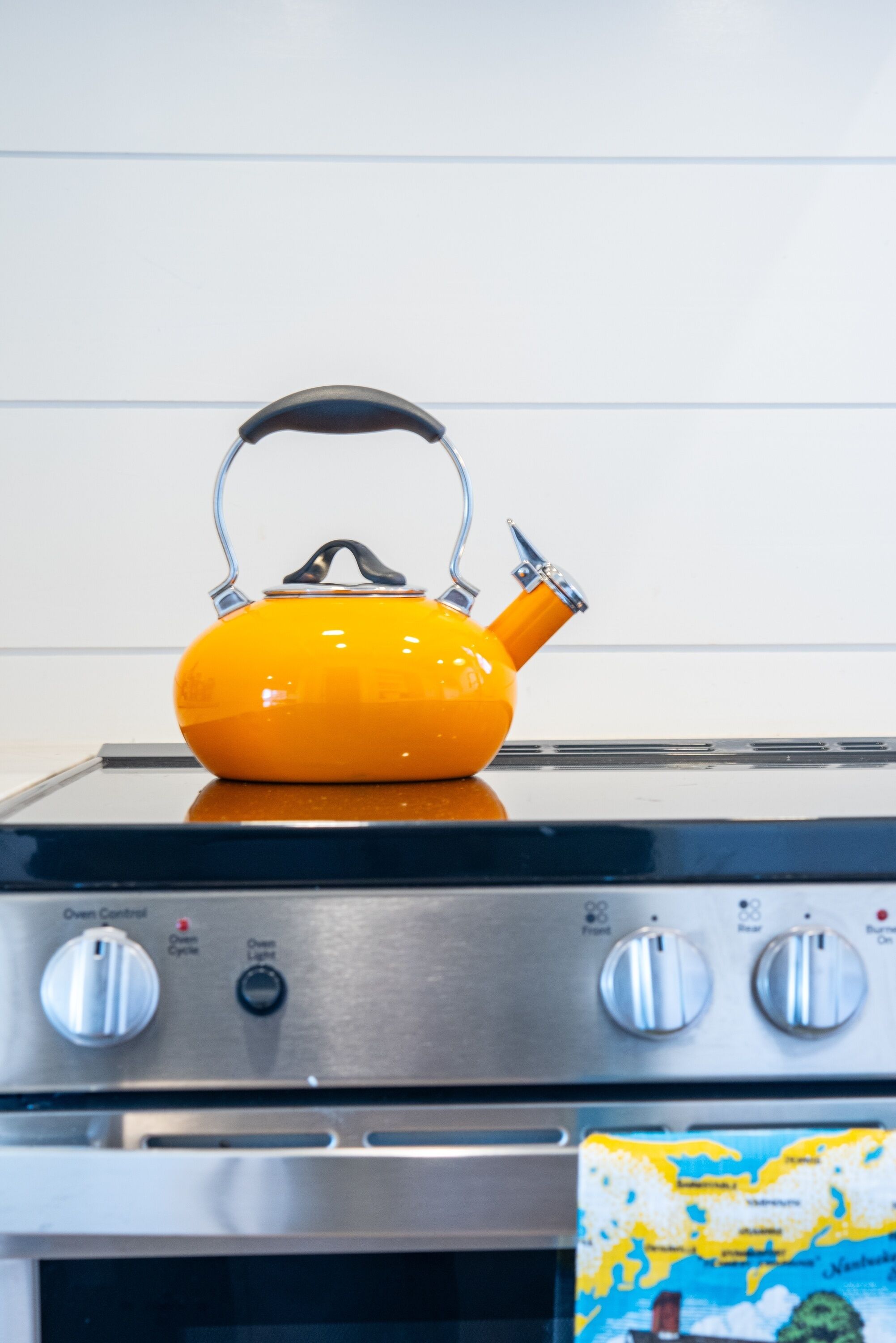 A kitchen with a yellow kettle on a stove, oven control knobs, and a map on the counter.