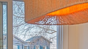 Une vue depuis une fenêtre donnant sur une terrasse en bois et une maison aux volets bleus.