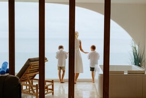 Una habitación con un ventanal arqueado que da al mar, una silla de madera y una bañera.