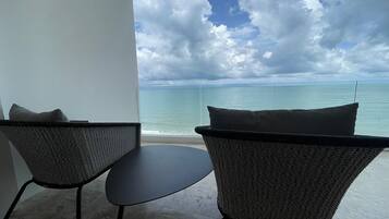 A balcony with two wicker chairs and a small table, overlooking a calm sea and a partly cloudy sky.