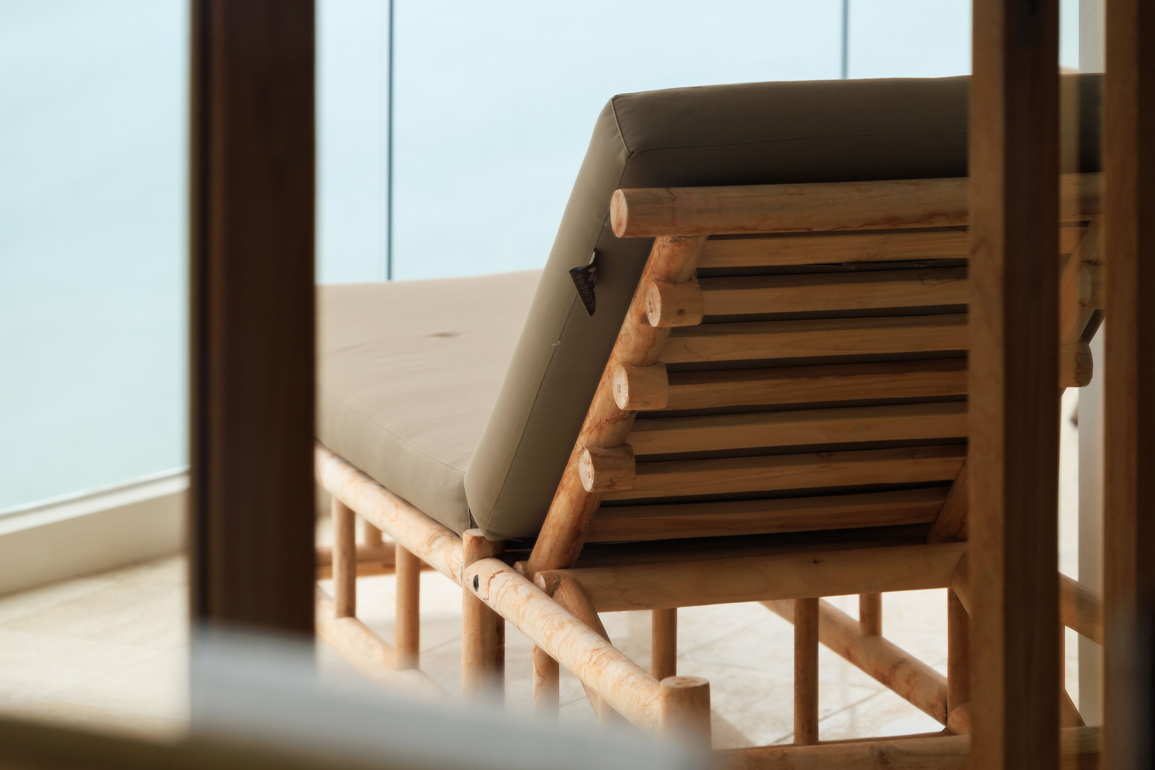 A wooden bench with a cushion, positioned indoors with a view of a light-colored wall.