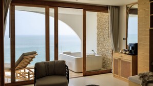 A modern room with a large sliding glass door leading to a balcony, a bathtub, a wooden cabinet, and a cushioned chair. - Elite Atoll Beachfront Hotel (Khanom)