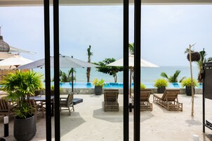 Un patio frente a la playa con sillones de descanso, sombrillas y plantas en macetas.