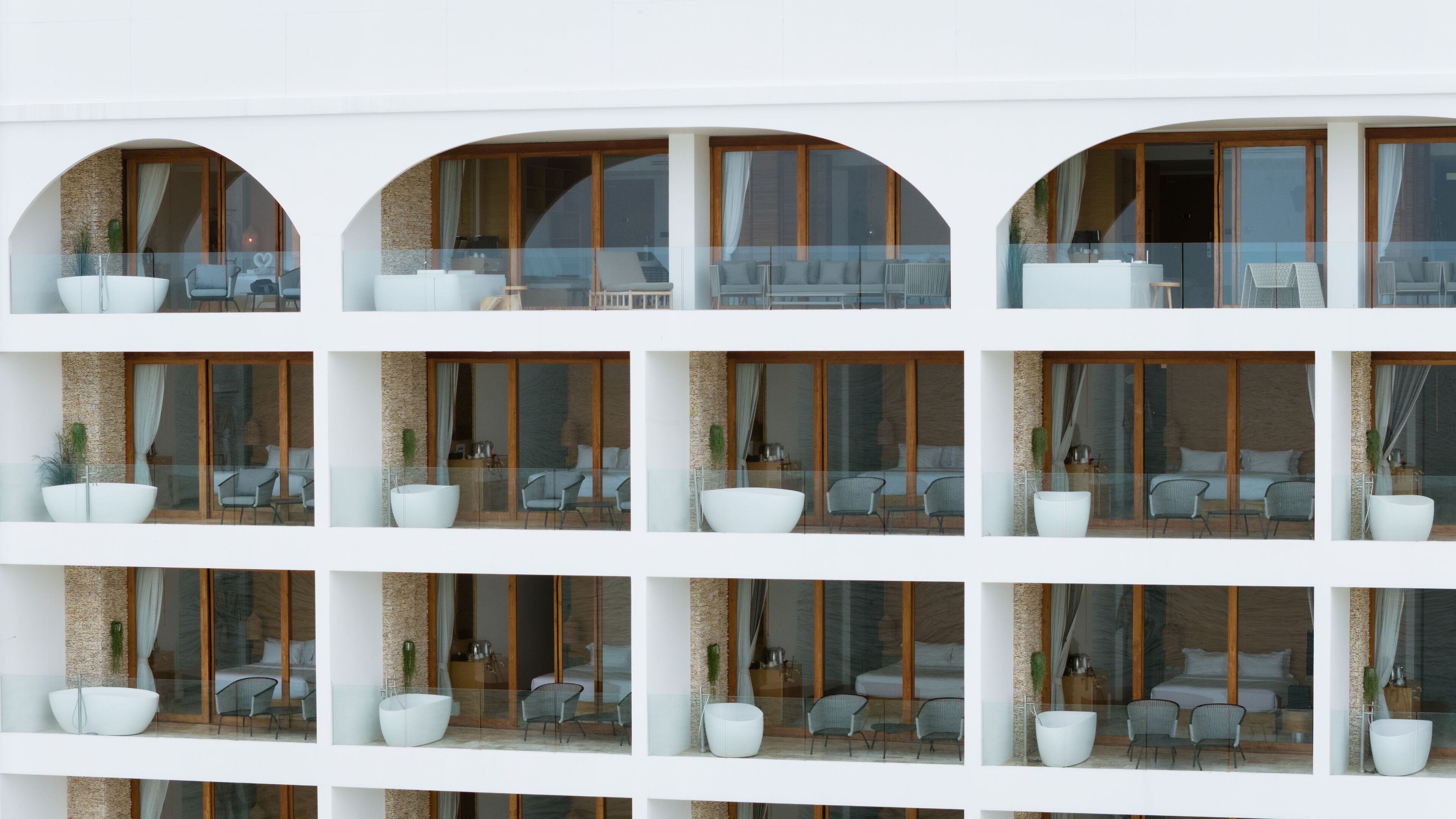 A multi-story hotel with balconies, each featuring a seating area with chairs and a large white bowl.
