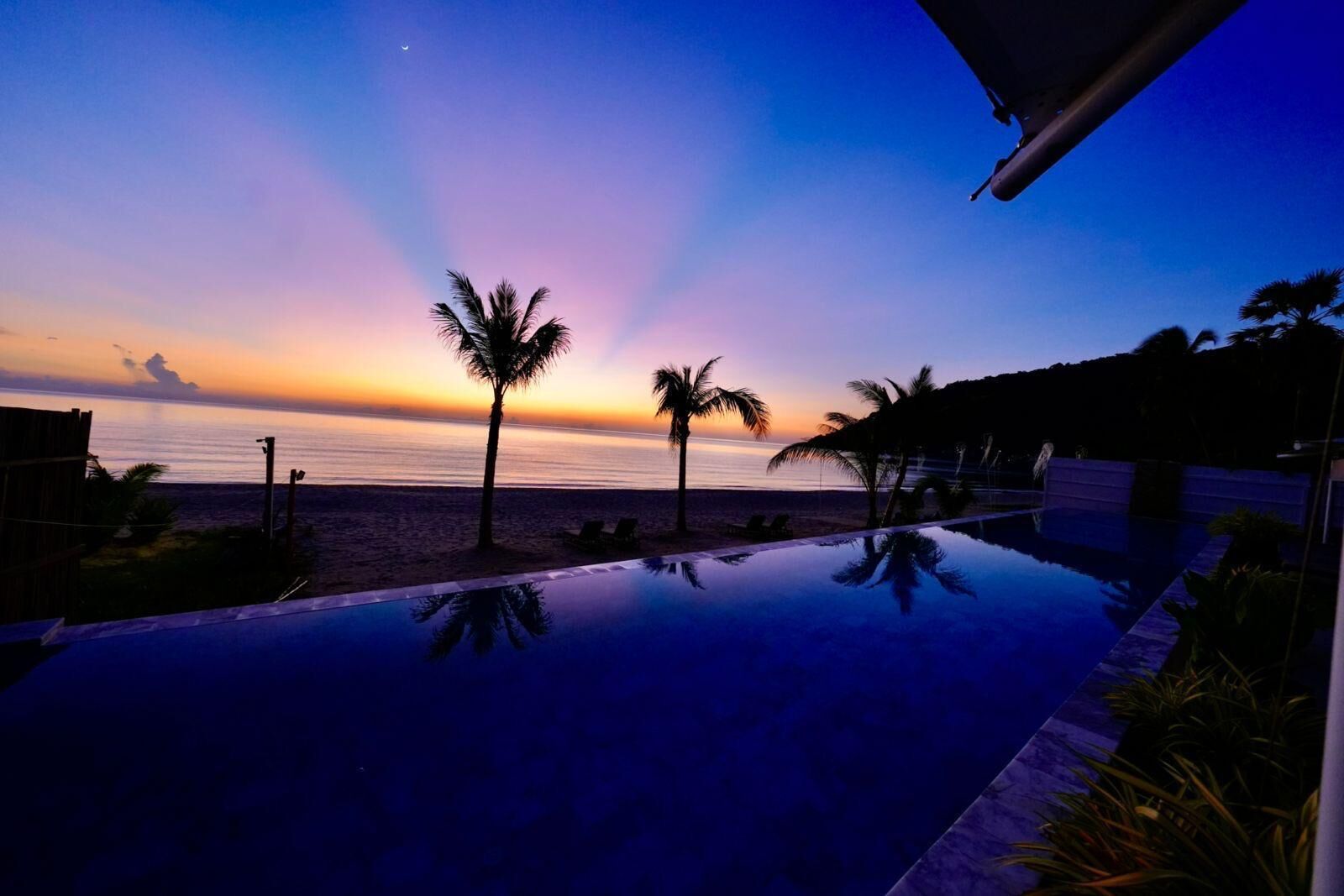 Una piscina con vista al océano y palmeras al atardecer.