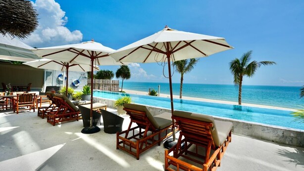 A poolside area with wooden lounge chairs and umbrellas, overlooking a clear blue ocean. - Elite Atoll Beachfront Hotel (Khanom)