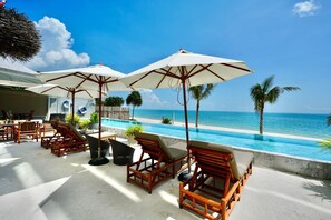 A poolside area with wooden lounge chairs and umbrellas, overlooking a clear blue ocean. - Elite Atoll Beachfront Hotel (Khanom)