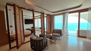 A modern hotel room with a balcony, a bed, a sofa, and a dining area. - Elite Atoll Beachfront Hotel (Khanom)