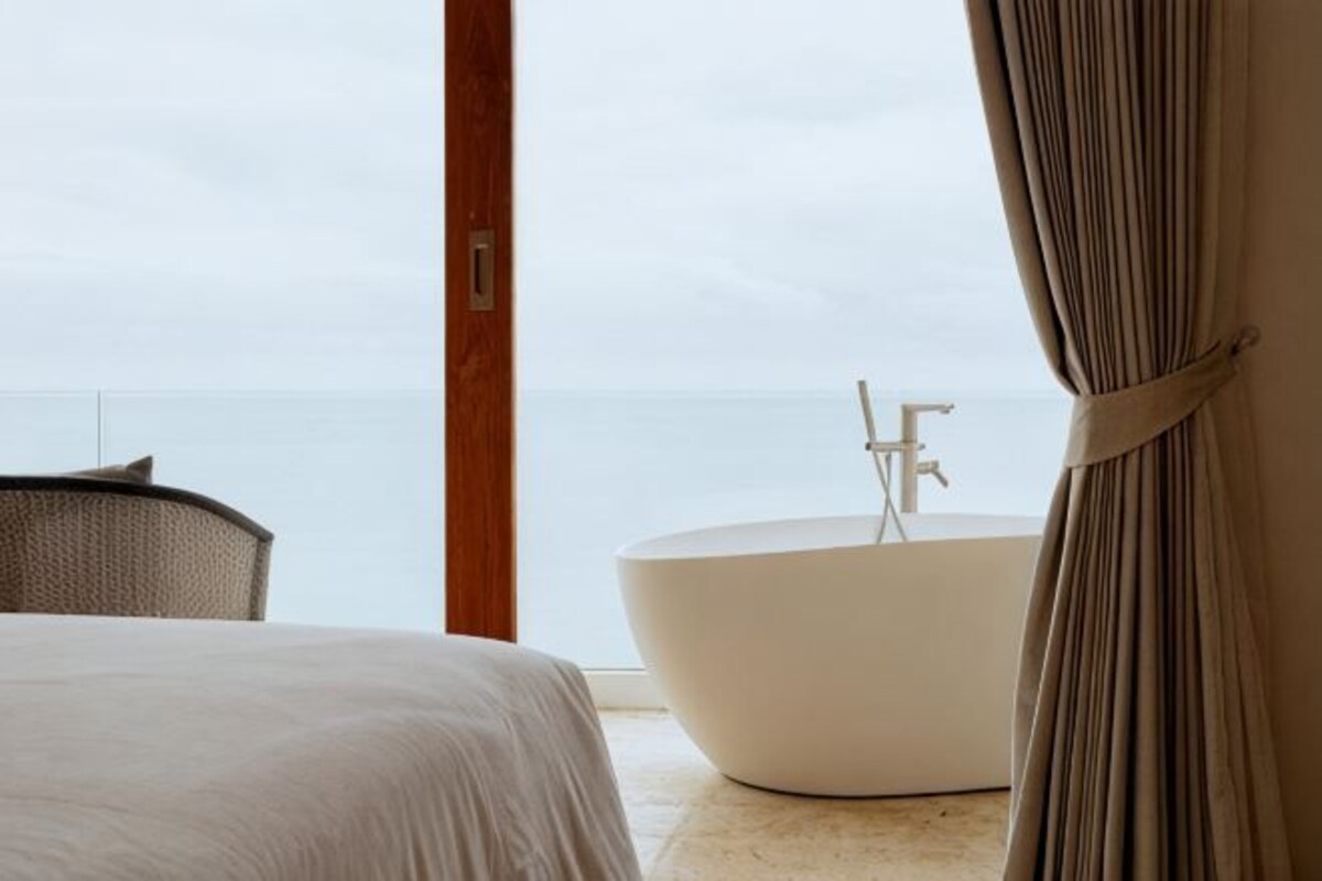 Een kamer met een bed, een groot bad en uitzicht op zee.
