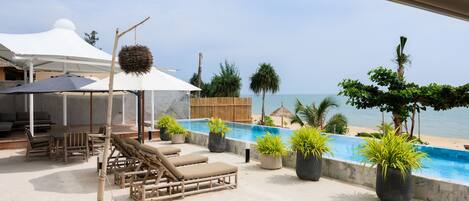 Zona junto a la piscina con sillones de descanso, plantas en macetas y vista a la playa.