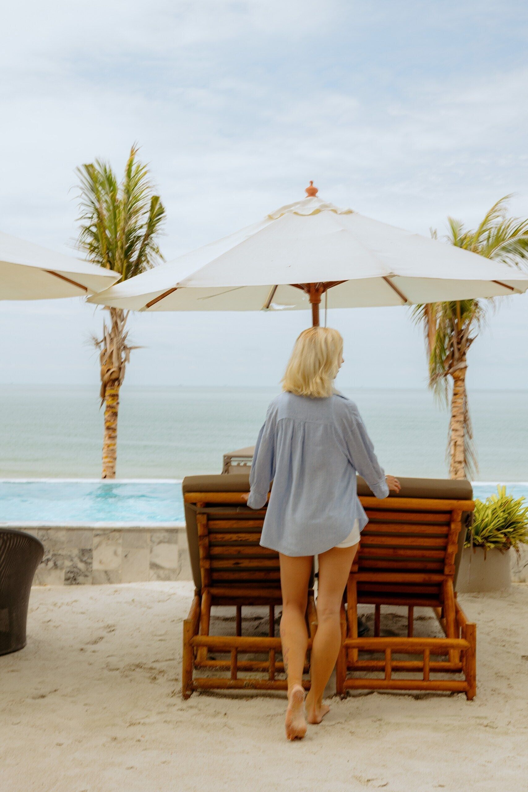 A person sitting at a wooden table with a beach view, under a large umbrella.