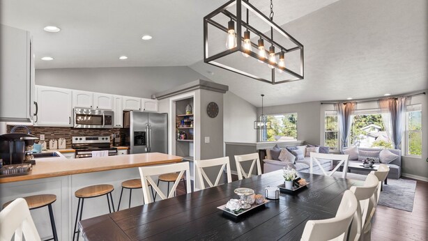 A modern kitchen with white cabinets, stainless steel appliances, and a dark wooden dining table with white chairs.