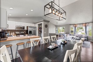 A modern kitchen with white cabinets, stainless steel appliances, and a dark wooden dining table with white chairs. - 6BR/3BA House - 2nd Living and Entry - 18 Guests (Spokane Valley)