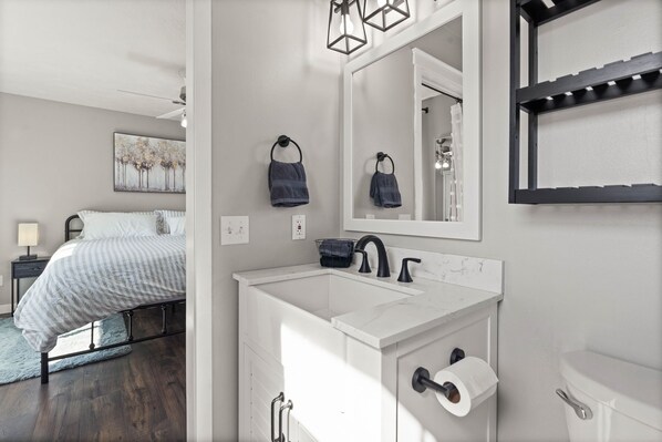 A modern bathroom with a white sink, black faucet, and a large mirror. There is a towel rack above the sink and a toilet paper holder next to it. - 6BR/3BA House - 2nd Living and Entry - 18 Guests (Spokane Valley)