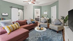 A living room with a pink sofa, a patterned armchair, a round coffee table, and a ceiling fan.