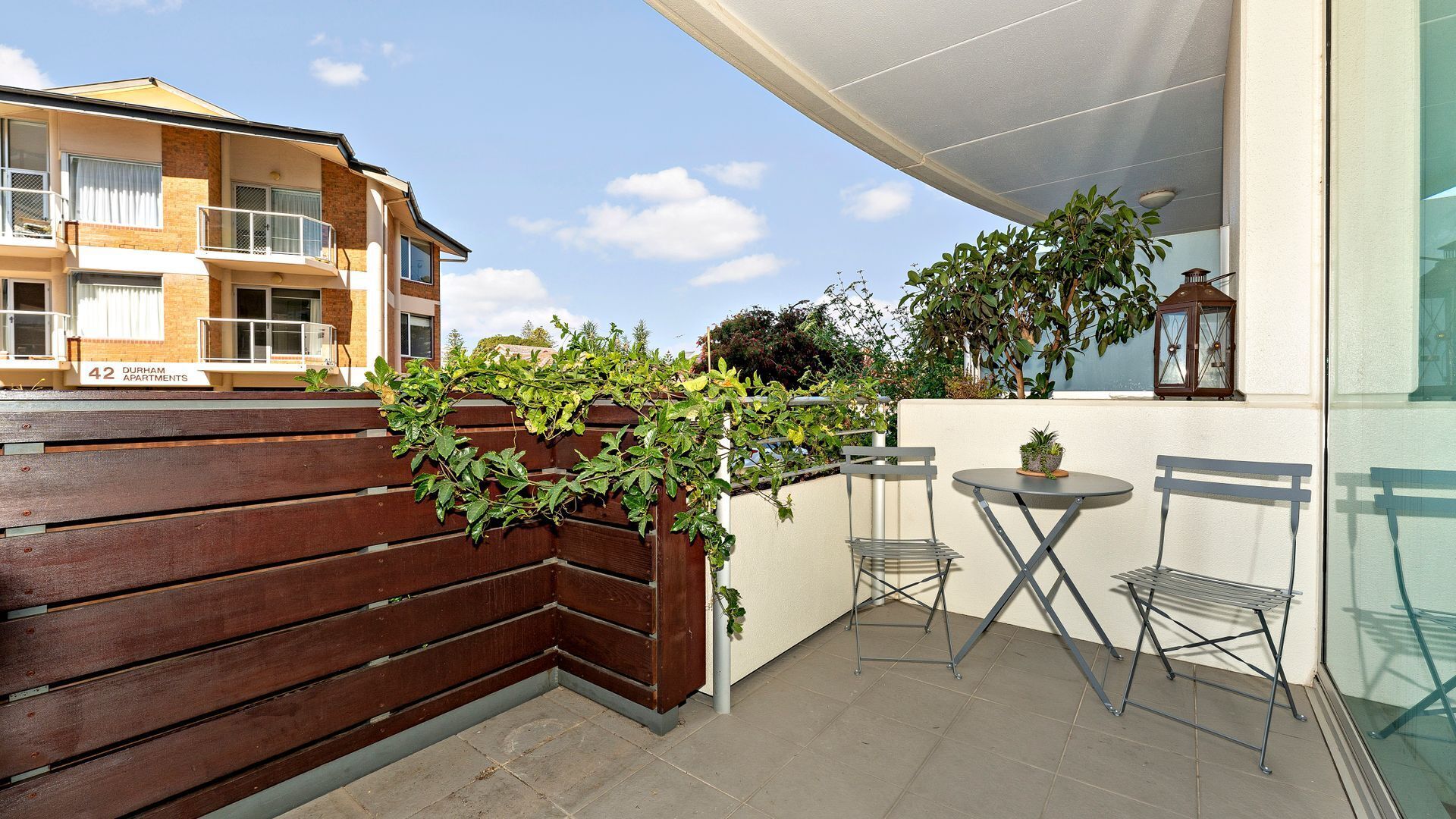 A balcony with a wooden fence, a small table, two chairs, and a potted plant.