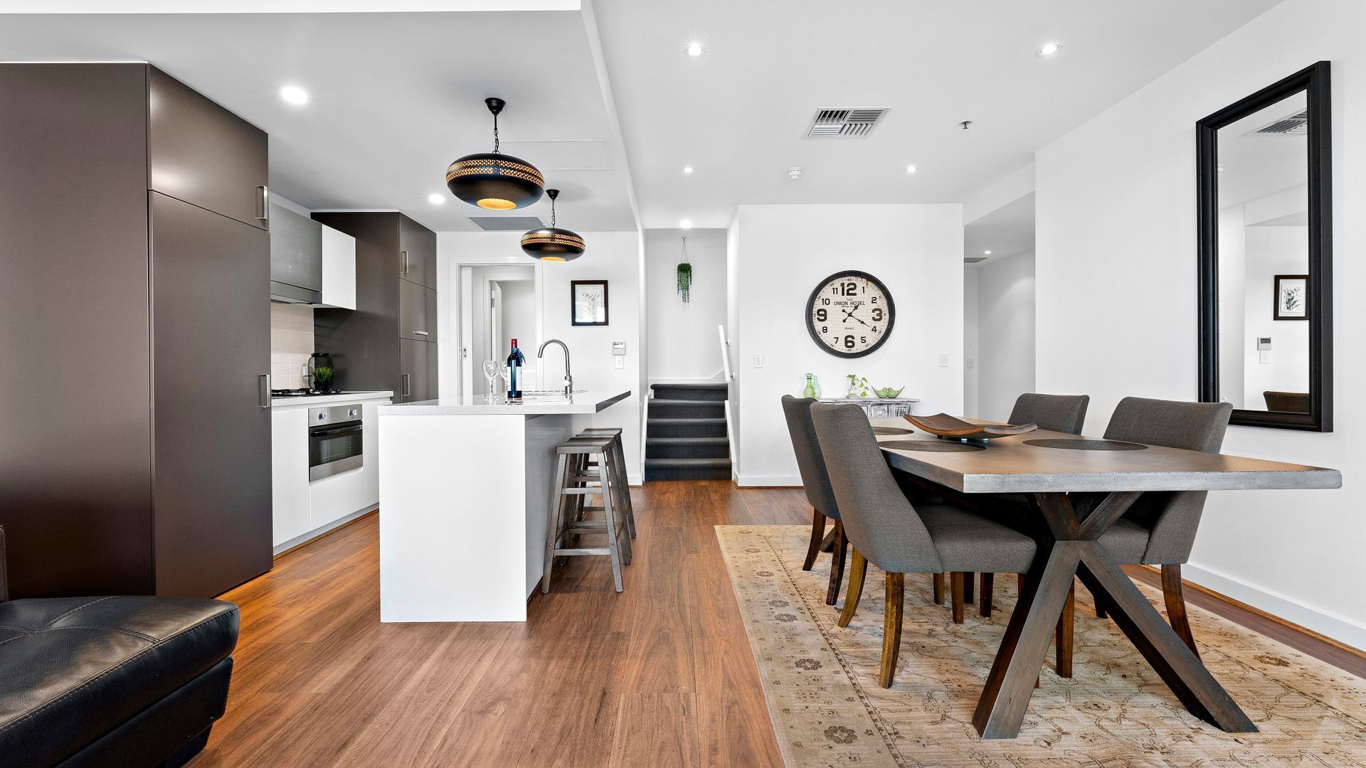 A modern kitchen with white cabinetry, a central island, and a dining area with a wooden table and grey chairs.