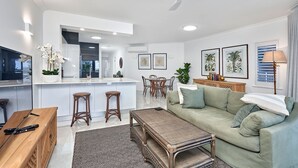 A modern living room with a green sofa, a coffee table, and a dining area with a table and chairs. - Coral Horizons Beachfront Apartment (Cairns)