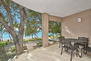 A covered patio with a table and chairs, overlooking a beach and trees. - Coral Horizons 604 | 2 Bedroom Apartment (Cairns)