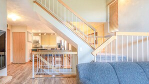 A spacious living area with a staircase leading to an upper level, a kitchen in the background, and a blue sofa. - Seven Springs 2BR Loft Premium Condo, sleeps 11! by RedAwning (Champion)