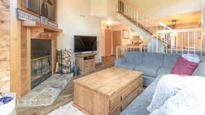 A cozy living room with a fireplace, a television, and a staircase leading to an upper level. - Seven Springs 2BR Loft Premium Condo, sleeps 11! by RedAwning (Champion)