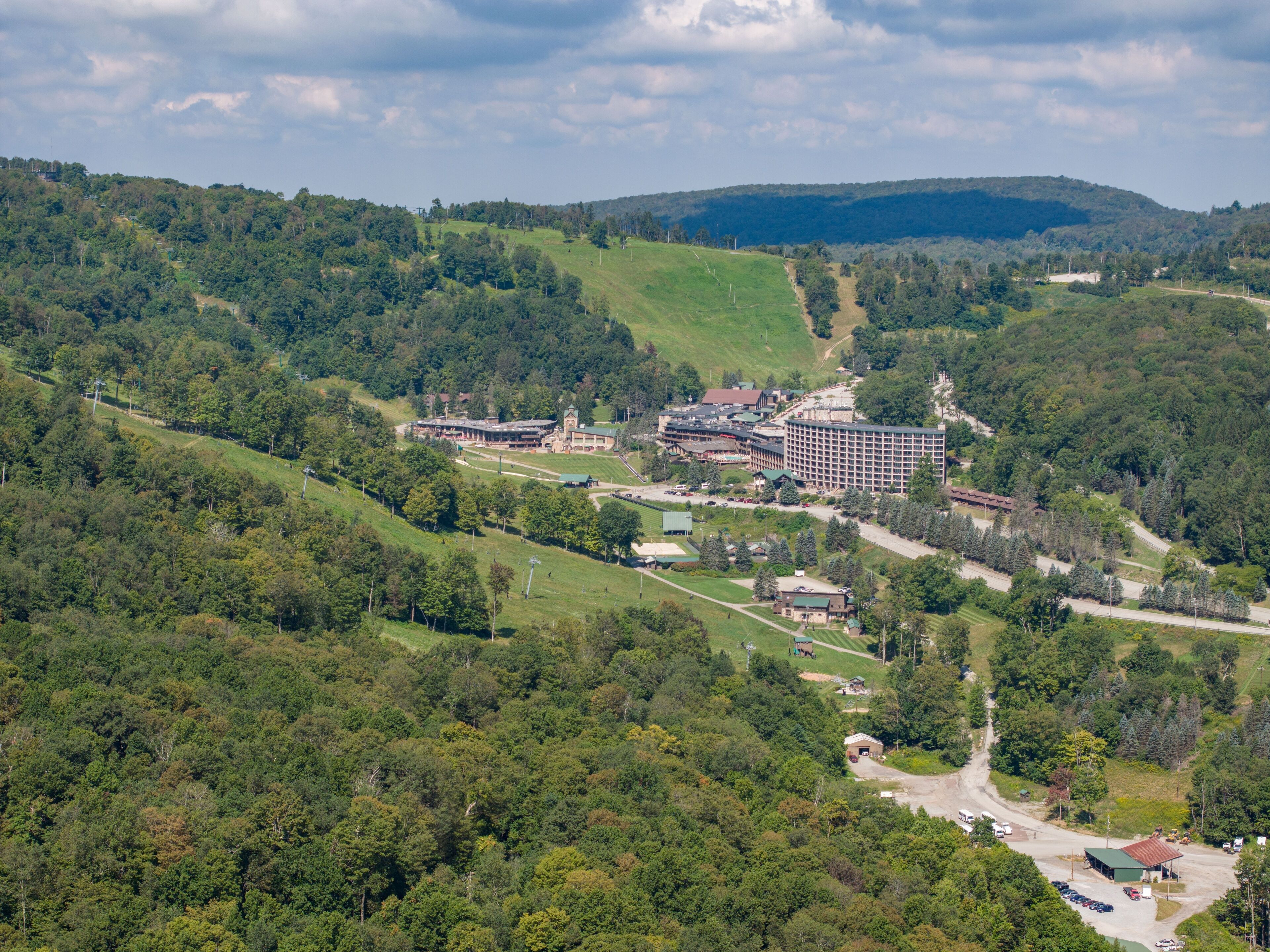 Un complexe hôtelier comprenant plusieurs bâtiments, entouré de collines verdoyantes et d’arbres.