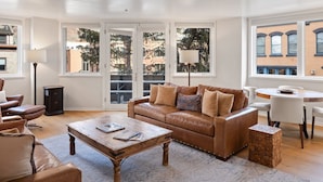 A living room with a brown leather sofa, a wooden coffee table, and a dining area with a white table and chairs. - Ice House 317 2 Bedroom Condo by RedAwning (Telluride)