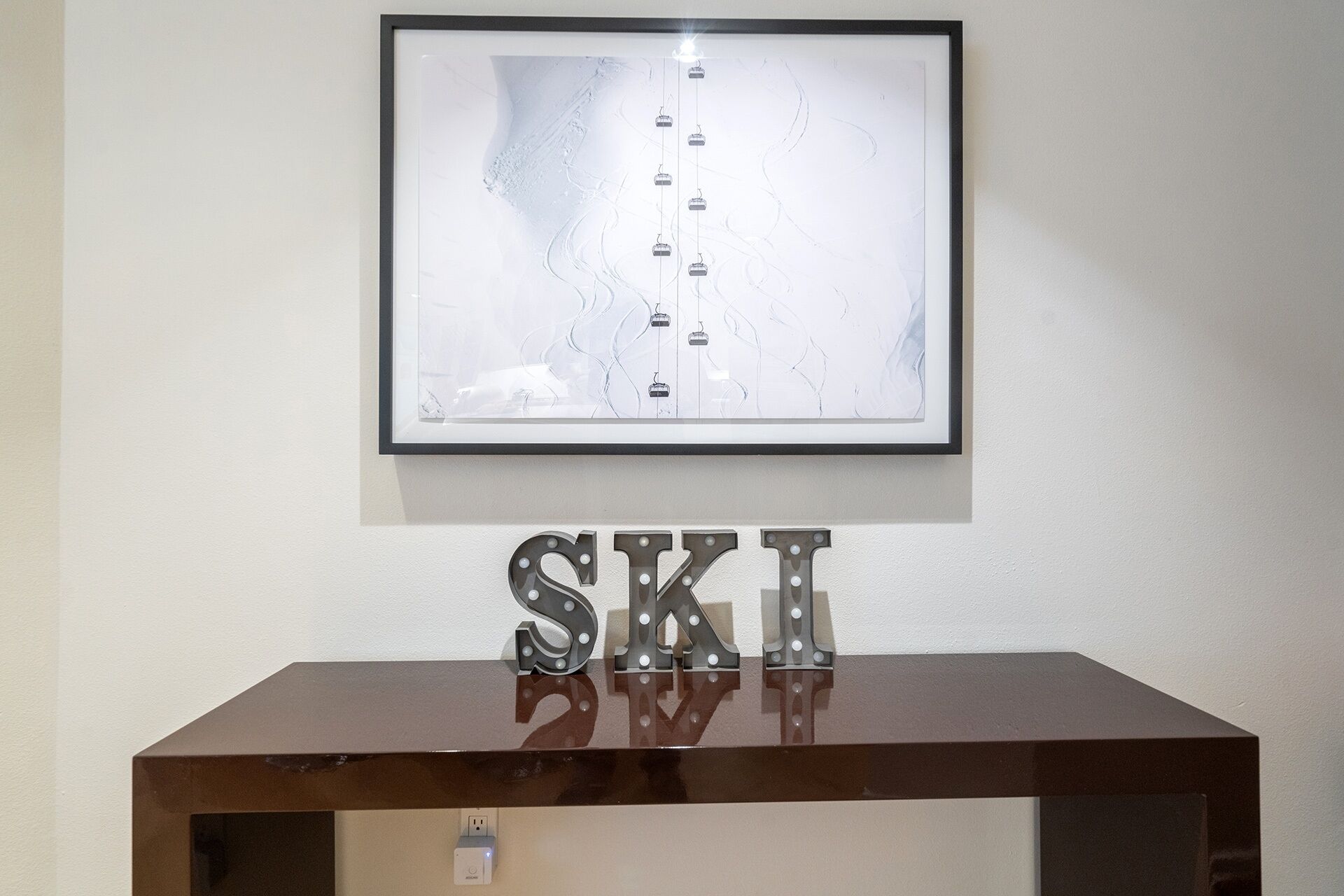 Una obra de arte enmarco con diseños abstractos y un letrero de metal con la palabra 'SKI' sobre una consola de madera oscura.