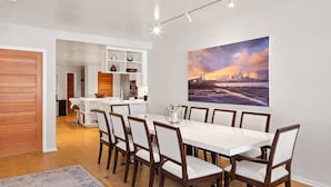 A modern dining area with a white table and wooden chairs, a kitchen in the background, and a large cityscape painting on the wall. - Ice House 317 2 Bedroom Condo by RedAwning (Telluride)