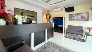 Un área de recepción con mostrador, sofá, televisor montado en la pared y un espejo decorativo.