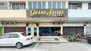 Un hotel llamado "Grand Safari Hotel" con una fachada moderna, unidades de aire acondicionado y un aparcamiento con varios coches y motocicletas.