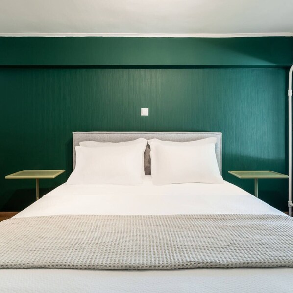 Una cama con sábanas y almohadas blancas, dos mesitas de noche y una pared verde.