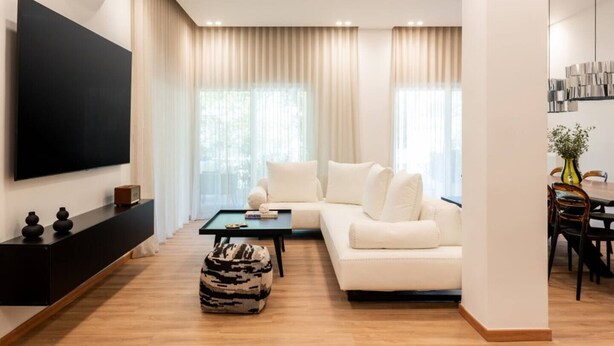 Un salon moderne comprenant un canapé d’angle, un téléviseur à écran plat, une table basse et un coin repas agrémenté d’un vase et de chaises.
