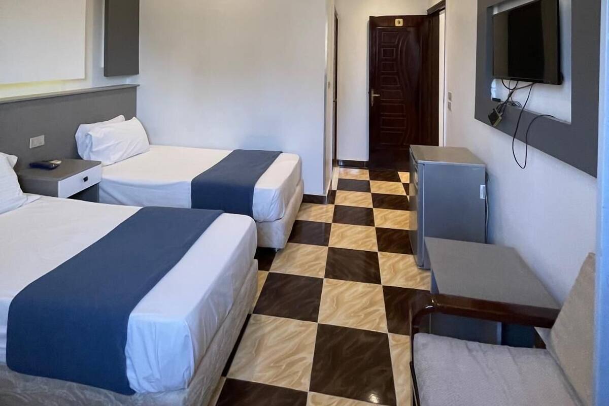 Une chambre d’hôtel avec deux lits, un bureau, une chaise, une télévision et un comptoir d’enregistrement.