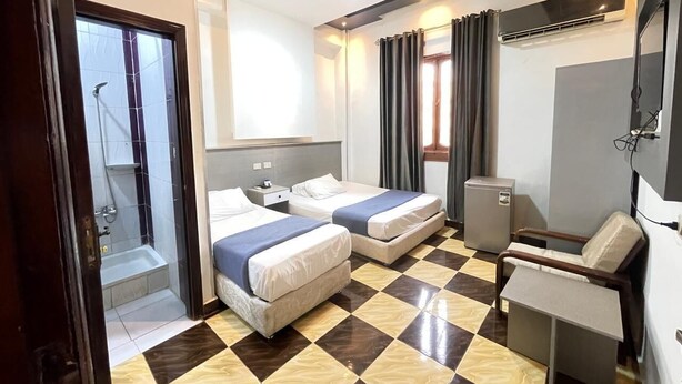 A hotel room with two beds, a desk, a chair, a small fridge, and a shower area. - Family Palace Downtown Cairo  (Cairo)