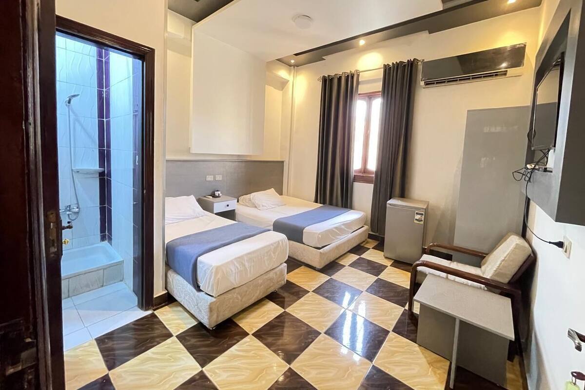 Une chambre d’hôtel avec deux lits, un bureau, une chaise, une douche et un grand miroir.