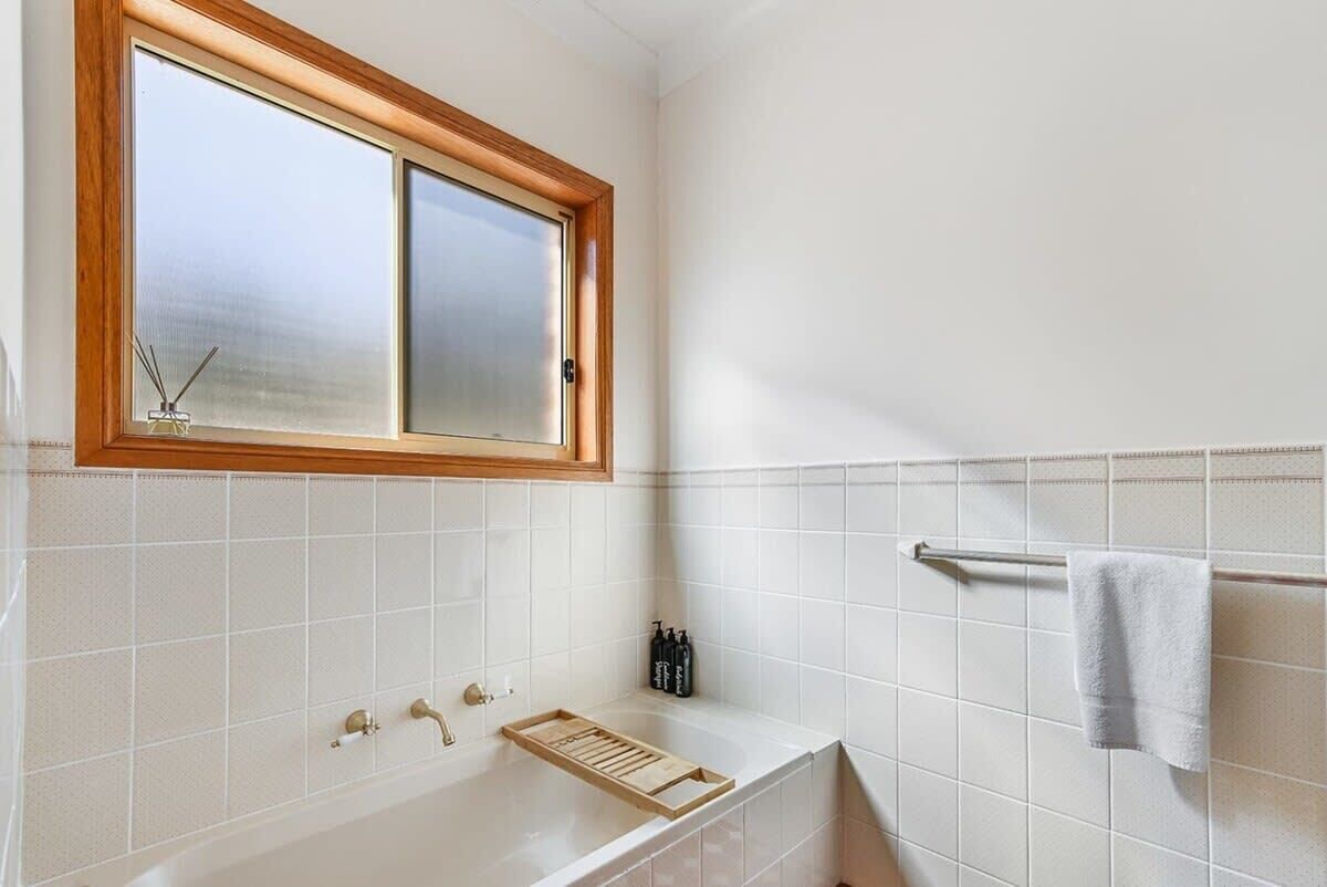 A bathroom with a bathtub, a window, a towel rack, and a shelf with toiletries.