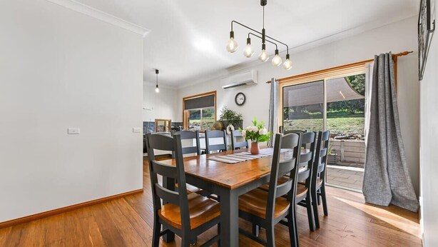 Un espace repas avec une table et des chaises en bois, un luminaire suspendu et une vue sur l’extérieur.